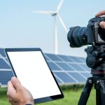 Journalist’s hands reviewing a blank tablet screen near solar panels and a wind turbine, symbolizing rigorous editorial standards in renewable energy reporting.